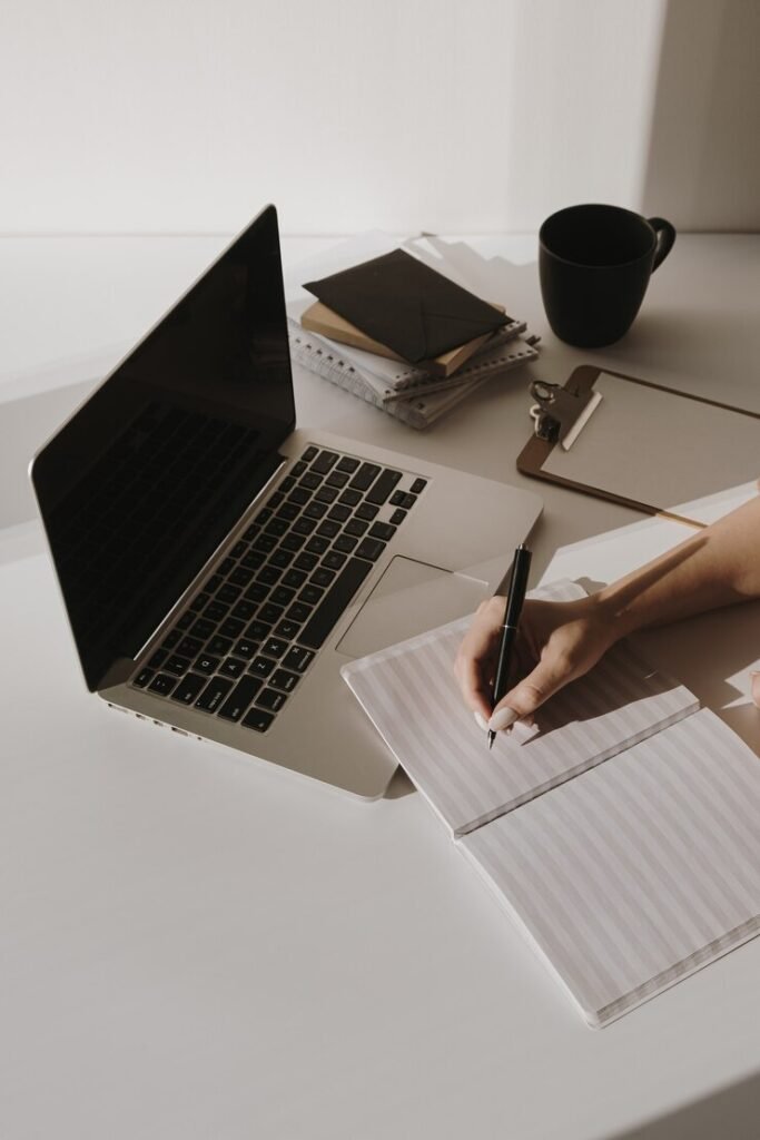 Minimalist home office workspace with a laptop, coffee cup, clipboard, and a person writing in a notebook, emphasizing productivity and organization for local business SEO strategies.