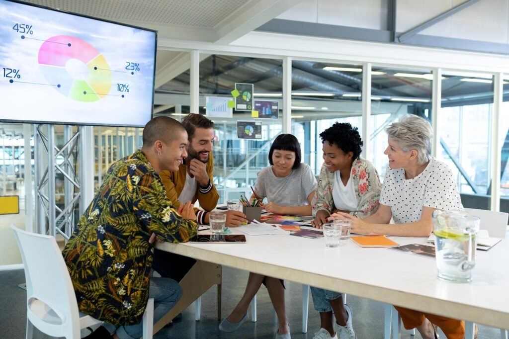 Group of diverse professionals collaborating at a table with documents and a pie chart on a screen, discussing strategies for local SEO and Google Business Profile optimization.