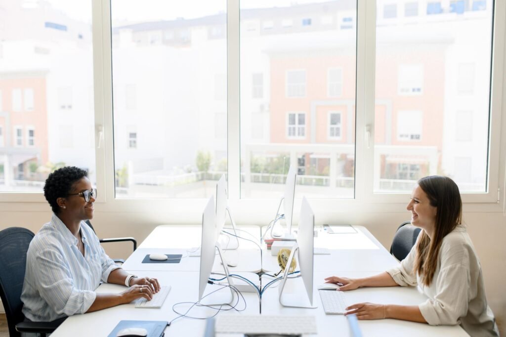 Two professionals collaborating in a modern office, smiling while working on computers, emphasising teamwork and productivity in Google Business Profile optimisation.
